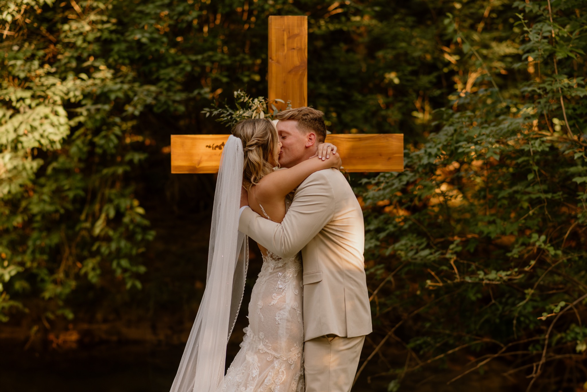 Newlyweds kissing beside the wooden cross in the Secret Garden at Blue Spring Estate
