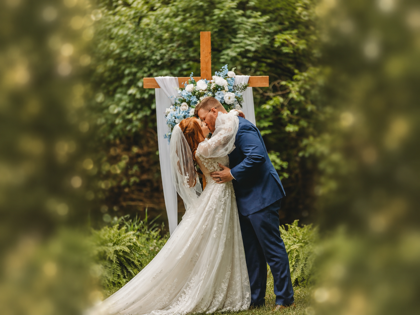 Newlyweds kissing beneath the floral cross in the Secret Garden at Blue Spring Estate
